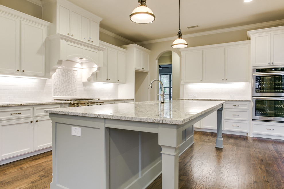 Photo of a large transitional l-shaped eat-in kitchen in Dallas with an undermount sink, shaker cabinets, white cabinets, granite benchtops, white splashback, subway tile splashback, stainless steel appliances, medium hardwood floors and with island.