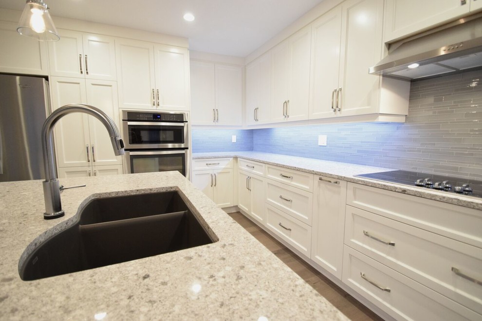 Inspiration for a transitional l-shaped vinyl floor and brown floor eat-in kitchen remodel in Edmonton with a double-bowl sink, shaker cabinets, white cabinets, quartz countertops, gray backsplash, glass tile backsplash, stainless steel appliances and an island