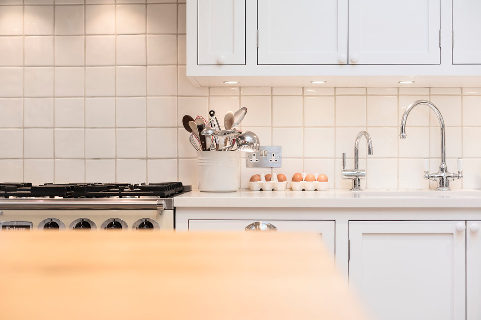 Large traditional u-shaped eat-in kitchen in London with a drop-in sink, shaker cabinets, white cabinets, solid surface benchtops, white splashback, ceramic splashback, coloured appliances, medium hardwood floors, with island, brown floor and beige benchtop.