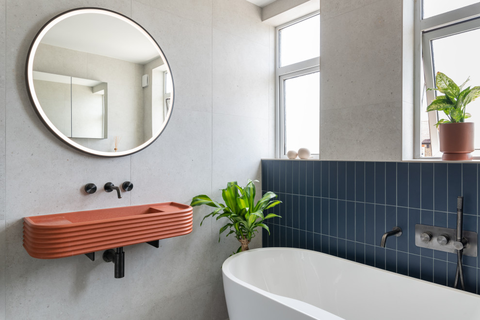 Пример оригинального дизайна: детская ванная комната среднего размера в современном стиле с отдельно стоящей ванной, открытым душем, унитазом-моноблоком, серой плиткой, керамогранитной плиткой, серыми стенами, полом из керамогранита, подвесной раковиной, столешницей из бетона, серым полом, душем с распашными дверями, оранжевой столешницей и тумбой под одну раковину