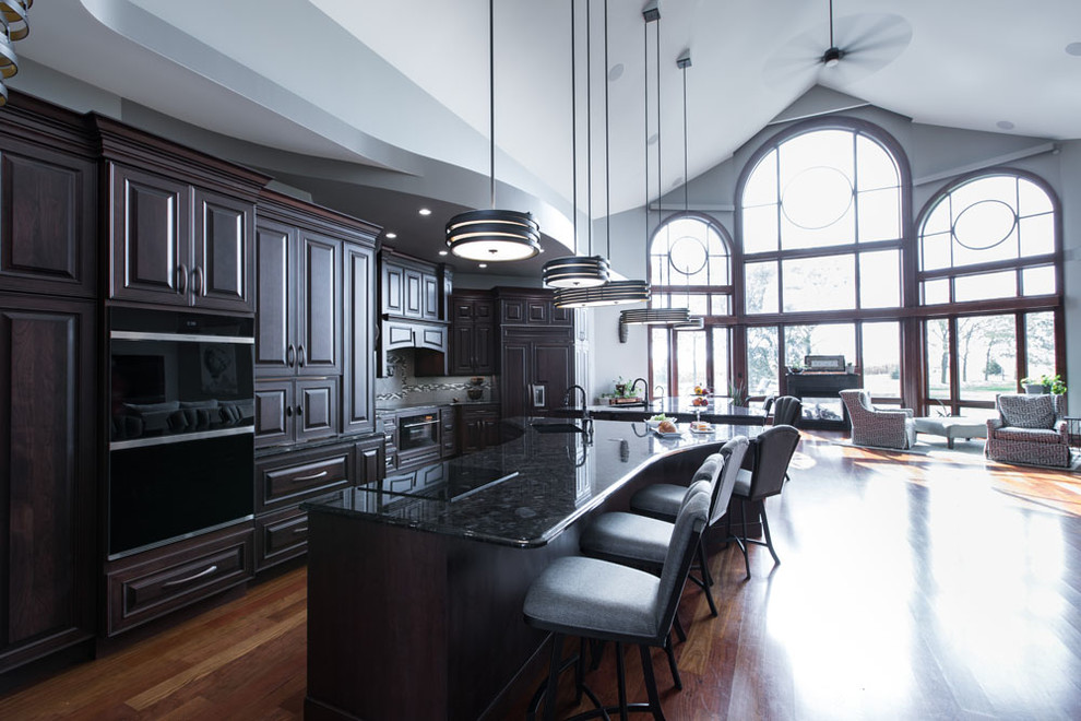 Transitional single-wall medium tone wood floor and brown floor eat-in kitchen photo with an undermount sink, raised-panel cabinets, dark wood cabinets, granite countertops, black appliances, two islands and black countertops