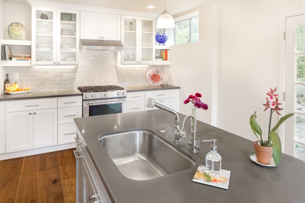 Inspiration for a mid-sized transitional l-shaped medium tone wood floor eat-in kitchen remodel with an undermount sink, glass-front cabinets, white cabinets, quartz countertops, gray backsplash, ceramic backsplash, stainless steel appliances and an island