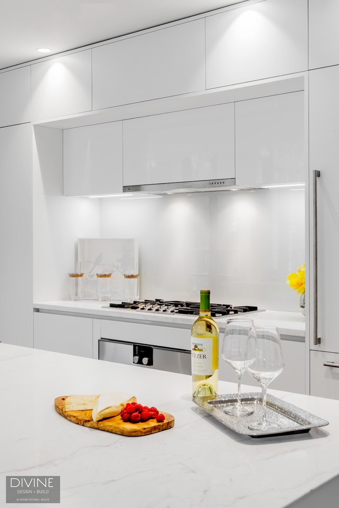 Design ideas for a large contemporary single-wall open plan kitchen in Boston with an undermount sink, flat-panel cabinets, white cabinets, quartz benchtops, white splashback, glass sheet splashback, panelled appliances, light hardwood floors, with island and beige floor.