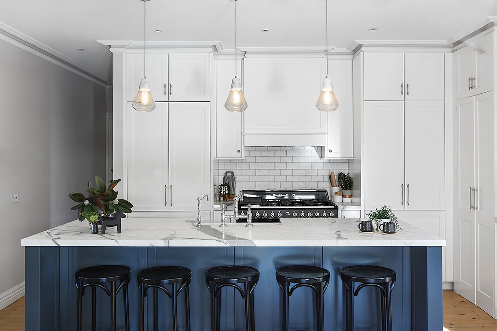 Inspiration for a transitional u-shaped kitchen in Melbourne with shaker cabinets, white cabinets, grey splashback, black appliances, medium hardwood floors, with island, brown floor and white benchtop.