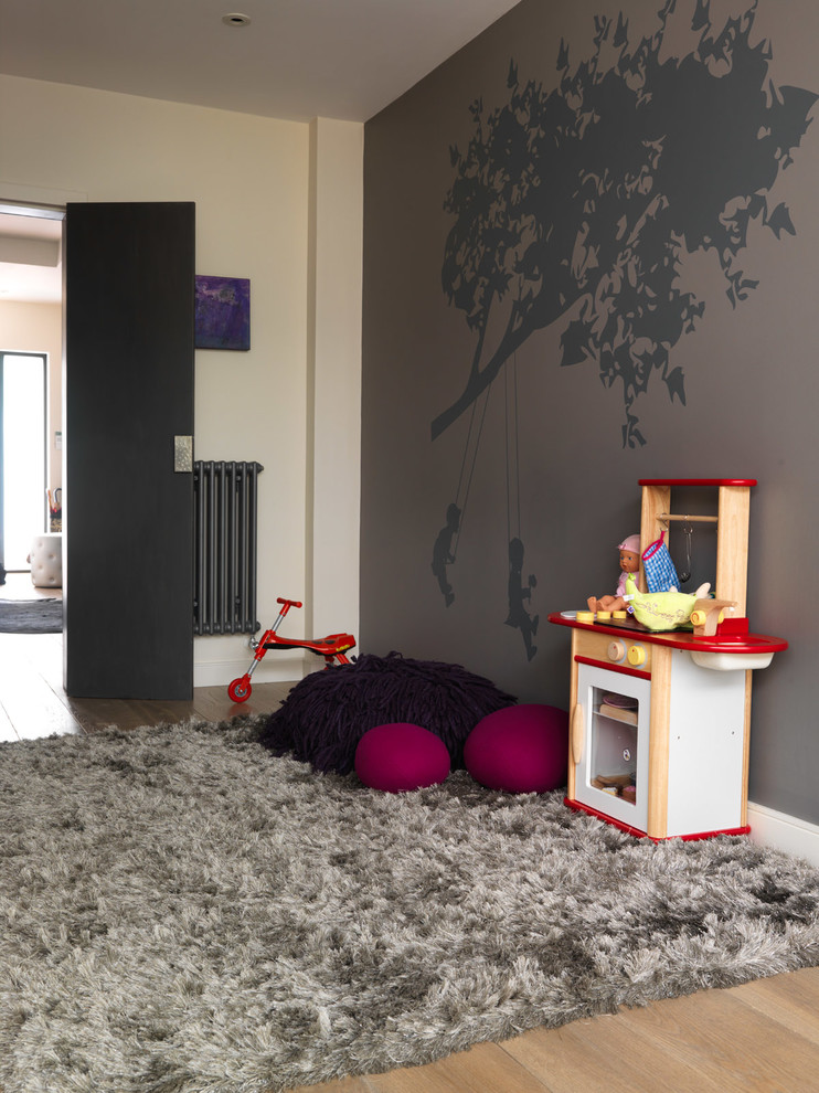 This is an example of a mid-sized contemporary gender-neutral kids' playroom for kids 4-10 years old in London with light hardwood floors and multi-coloured walls.