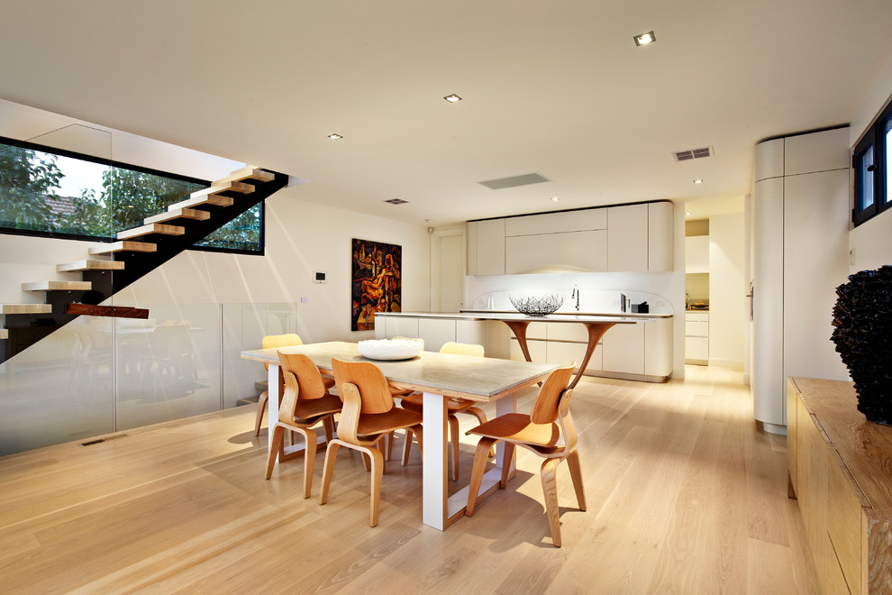 Photo of a contemporary galley open plan kitchen in Melbourne with an integrated sink, flat-panel cabinets, white cabinets, solid surface benchtops, white splashback and stone slab splashback.
