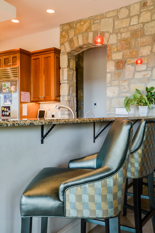 Open concept kitchen - mid-sized transitional l-shaped travertine floor open concept kitchen idea in Austin with an undermount sink, shaker cabinets, medium tone wood cabinets, granite countertops, beige backsplash, stone tile backsplash, stainless steel appliances and an island