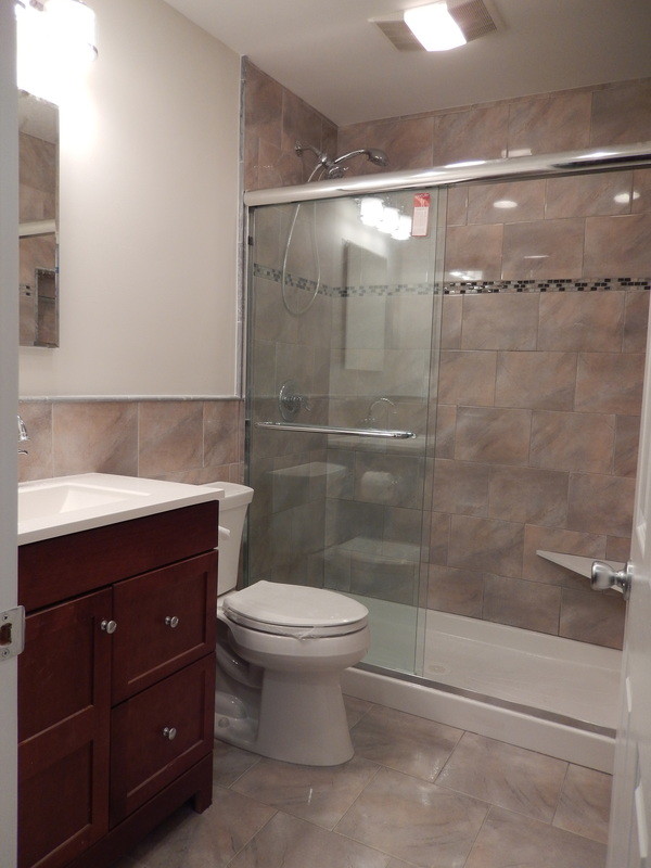 This is an example of a small 3/4 bathroom in New York with an integrated sink, flat-panel cabinets, dark wood cabinets, engineered quartz benchtops, an alcove shower, a two-piece toilet, brown tile, ceramic tile, brown walls and ceramic floors.