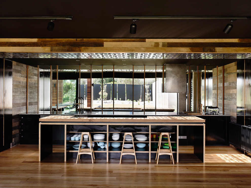 Inspiration for a large contemporary galley open plan kitchen in Melbourne with an undermount sink, open cabinets, black cabinets, mirror splashback, with island, wood benchtops, black splashback, black appliances and medium hardwood floors.