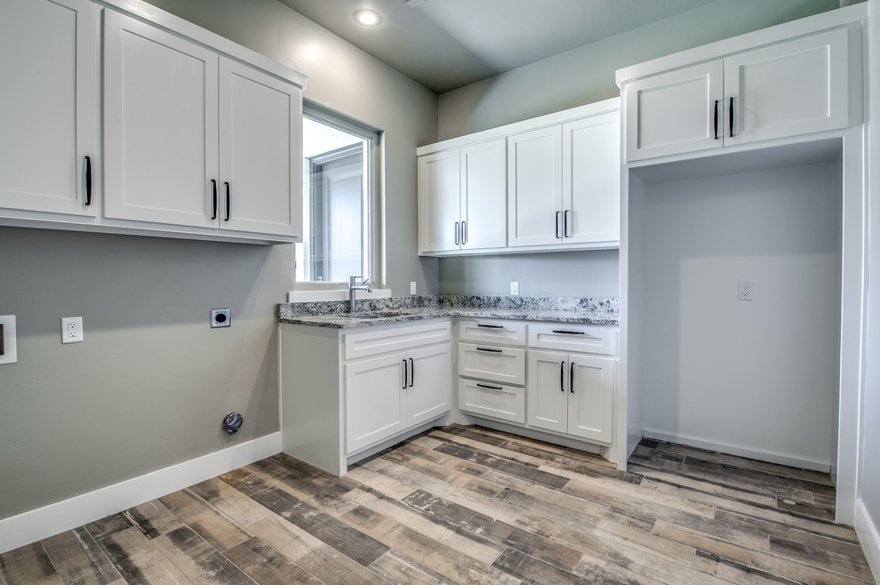 This is an example of a transitional l-shaped laundry room in Austin with a single-bowl sink, shaker cabinets, white cabinets, granite benchtops, grey walls, medium hardwood floors, a side-by-side washer and dryer and beige floor.