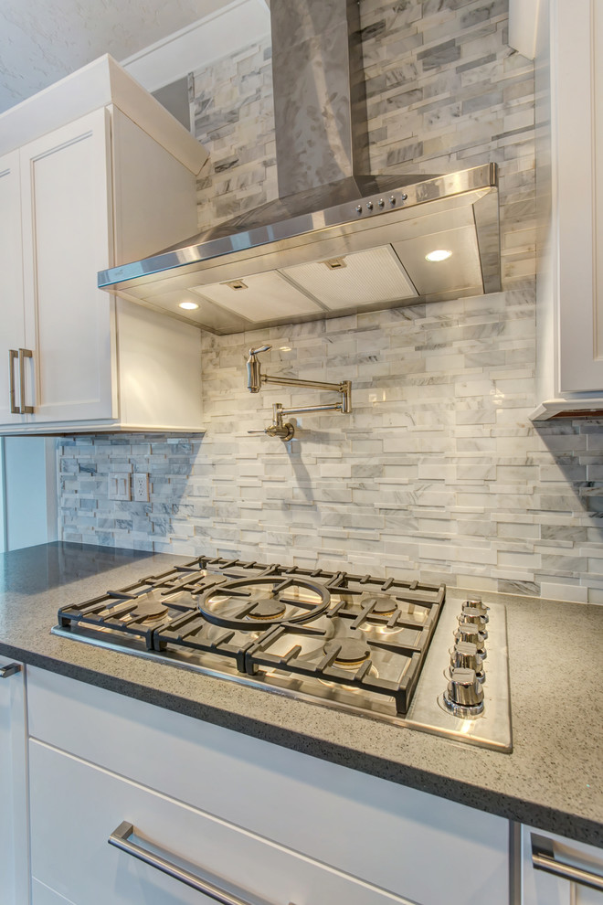 Example of a mid-sized transitional l-shaped medium tone wood floor open concept kitchen design in Seattle with an undermount sink, shaker cabinets, white cabinets, quartz countertops, gray backsplash, stone tile backsplash, stainless steel appliances and an island