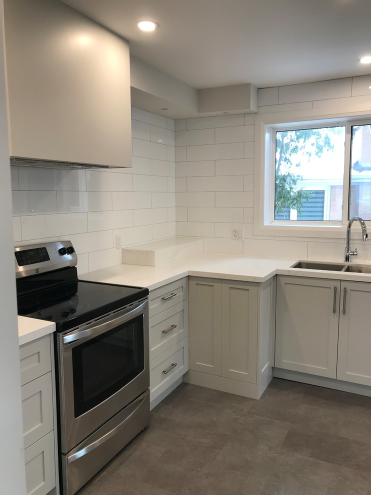 Example of a mid-sized transitional porcelain tile and brown floor home design design in Toronto with an undermount sink, shaker cabinets, gray cabinets, quartz countertops, white backsplash, subway tile backsplash, stainless steel appliances, an island and white countertops
