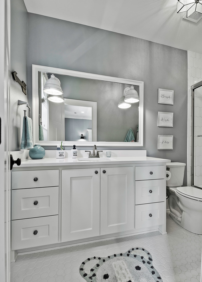 This is an example of a large arts and crafts kids bathroom in Other with raised-panel cabinets, white cabinets, a shower/bathtub combo, a two-piece toilet, white tile, grey walls, mosaic tile floors, an undermount sink, engineered quartz benchtops, white floor, a sliding shower screen and white benchtops.
