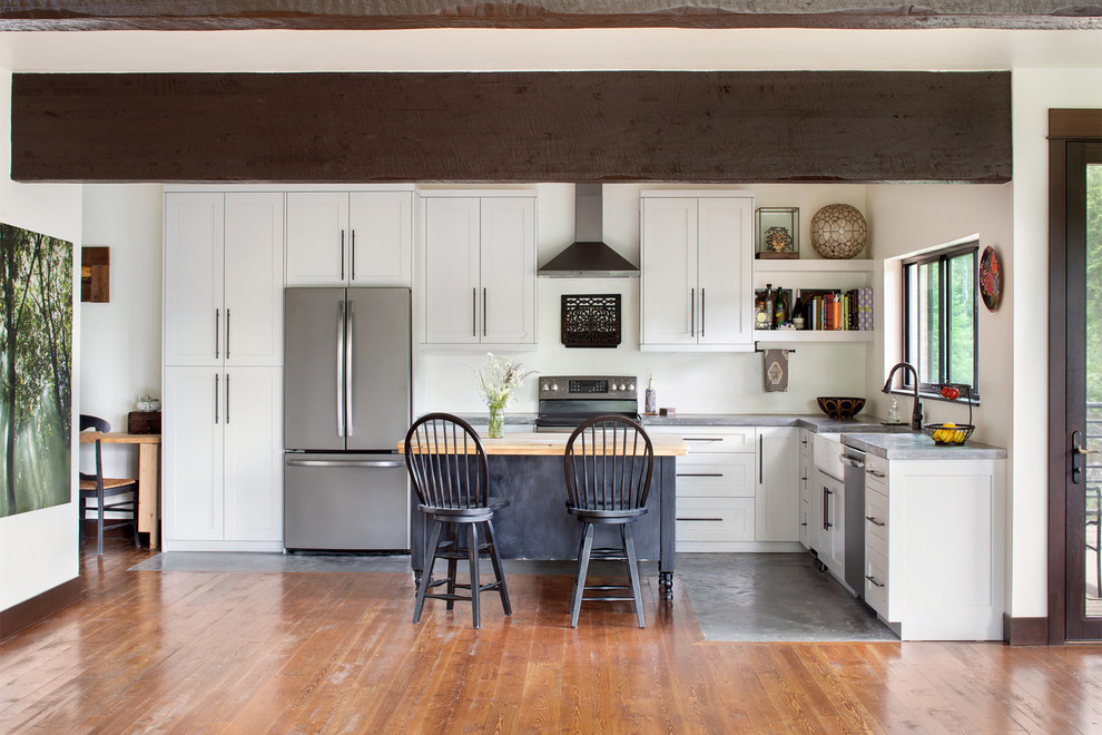 Example of a transitional l-shaped concrete floor and gray floor kitchen design with a farmhouse sink, shaker cabinets, white cabinets, stainless steel appliances, an island and gray countertops