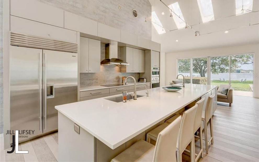 Photo of a large modern single-wall open plan kitchen in Tampa with an undermount sink, flat-panel cabinets, beige cabinets, quartzite benchtops, beige splashback, stone tile splashback, stainless steel appliances, laminate floors, multiple islands, beige floor, white benchtop and vaulted.