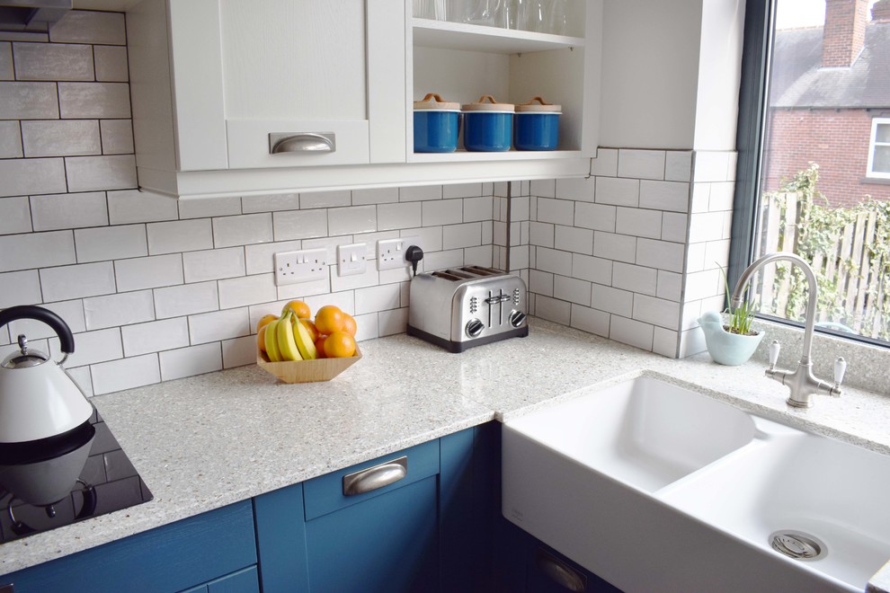 This is an example of a mid-sized contemporary u-shaped eat-in kitchen in Other with a farmhouse sink, shaker cabinets, blue cabinets, recycled glass benchtops, white splashback, ceramic splashback, linoleum floors, a peninsula and grey floor.