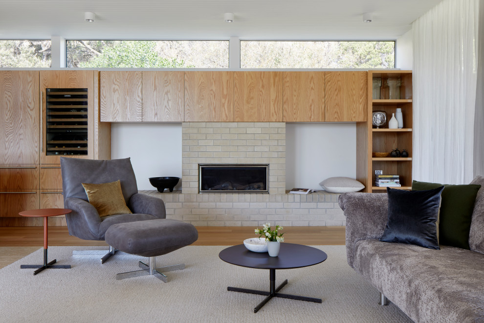 Photo of a large contemporary formal open concept living room in Melbourne with white walls, medium hardwood floors, a standard fireplace, a brick fireplace surround, no tv, brown floor and timber.
