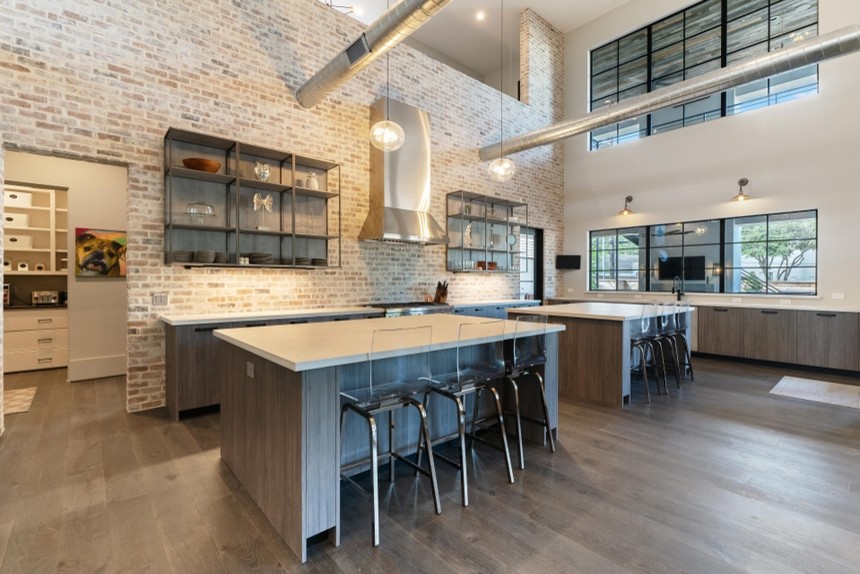 Large industrial u-shaped open plan kitchen in Houston with an undermount sink, flat-panel cabinets, distressed cabinets, quartz benchtops, multi-coloured splashback, terra-cotta splashback, stainless steel appliances, painted wood floors, multiple islands, brown floor and grey benchtop.