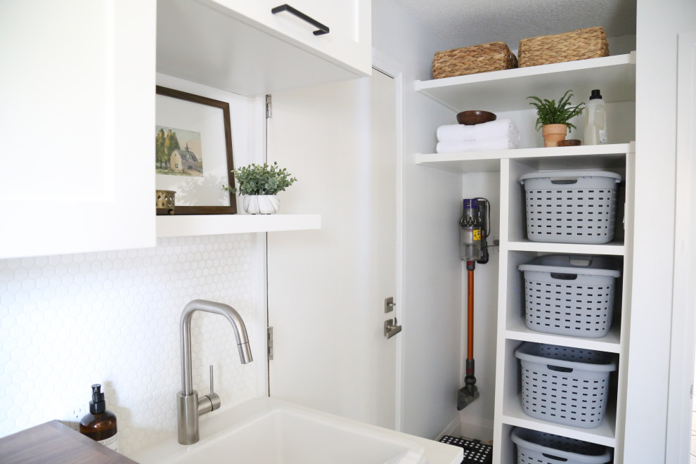 Inspiration for a mid-sized scandinavian galley utility room in Toronto with a drop-in sink, shaker cabinets, white cabinets, wood benchtops, white walls, porcelain floors, a side-by-side washer and dryer, black floor and brown benchtop.