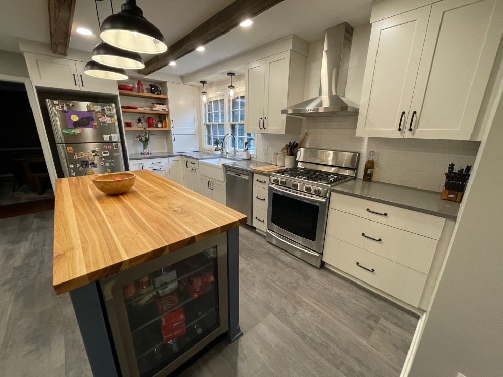 Enclosed kitchen - mid-sized cottage l-shaped gray floor and exposed beam enclosed kitchen idea in Detroit with a farmhouse sink, shaker cabinets, white cabinets, quartz countertops, white backsplash, subway tile backsplash, stainless steel appliances, an island and gray countertops