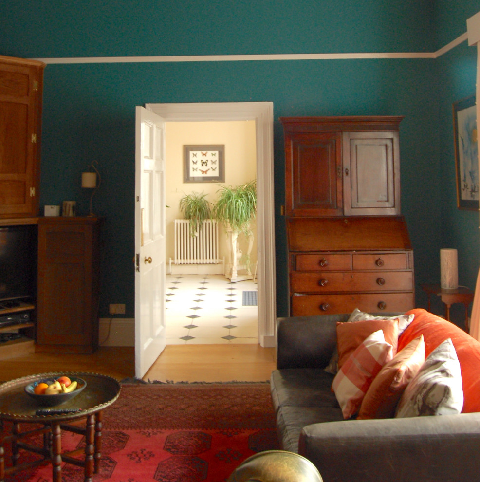 На фото: большая гостиная комната в стиле кантри с синими стенами, паркетным полом среднего тона, печью-буржуйкой, фасадом камина из камня, отдельно стоящим телевизором и зоной отдыха
