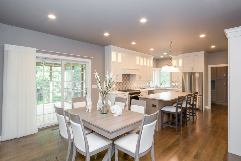 Mid-sized transitional l-shaped medium tone wood floor and brown floor eat-in kitchen photo in Cedar Rapids with a double-bowl sink, recessed-panel cabinets, white cabinets, quartz countertops, multicolored backsplash, porcelain backsplash, stainless steel appliances, an island and white countertops