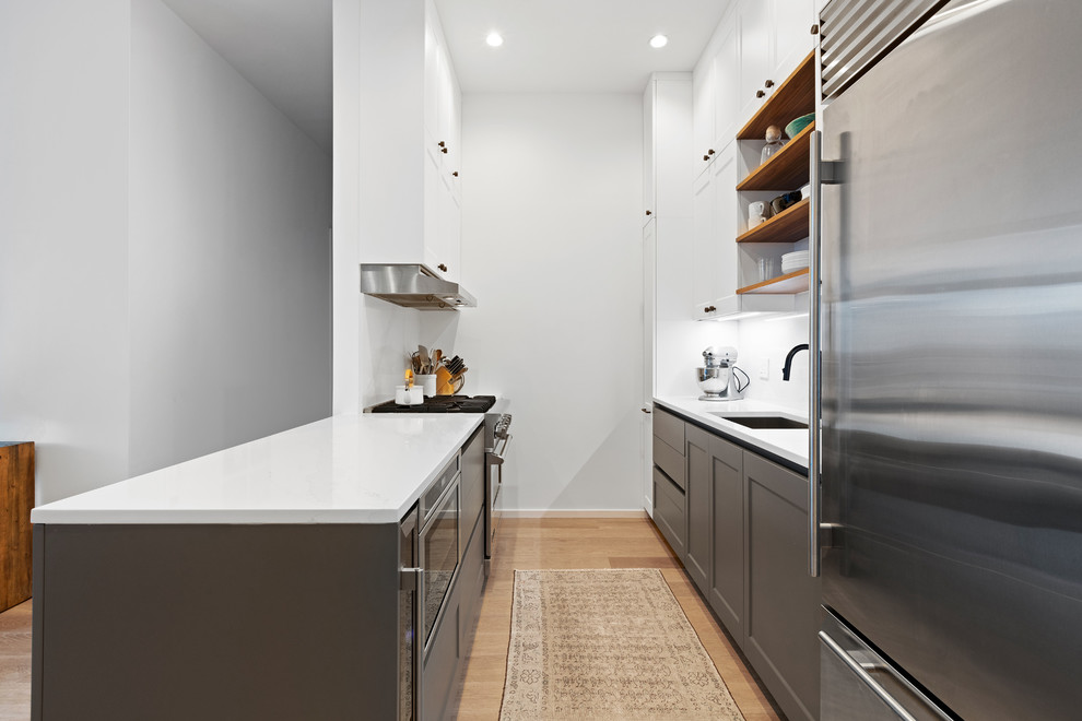 Inspiration for a mid-sized transitional galley separate kitchen in New York with an undermount sink, recessed-panel cabinets, grey cabinets, quartz benchtops, white splashback, stone slab splashback, stainless steel appliances, medium hardwood floors, a peninsula and white benchtop.