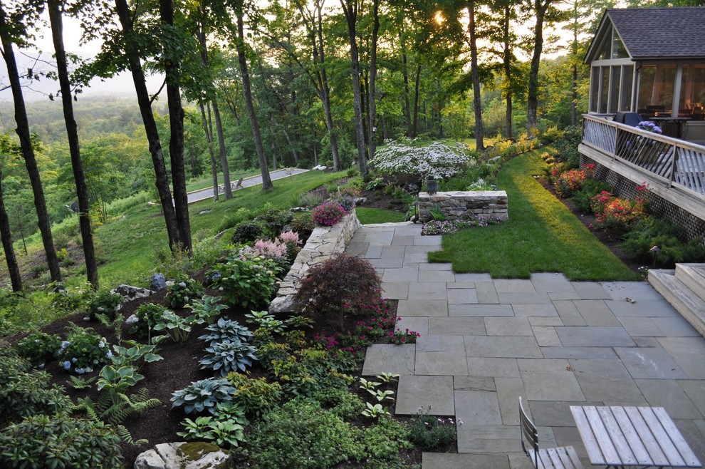 Photo of a large traditional backyard partial sun garden for spring in Boston with a retaining wall and natural stone pavers.