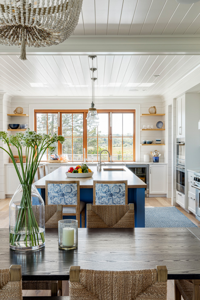 Photo of a large beach style l-shaped eat-in kitchen in Boston with a single-bowl sink, recessed-panel cabinets, white cabinets, granite benchtops, blue splashback, glass tile splashback, stainless steel appliances, medium hardwood floors, with island, white benchtop and timber.
