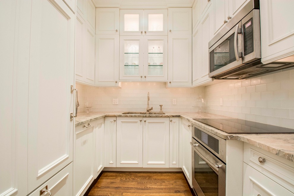 This is an example of a mid-sized traditional u-shaped separate kitchen in Boston with an undermount sink, raised-panel cabinets, white cabinets, granite benchtops, white splashback, porcelain splashback, stainless steel appliances, medium hardwood floors and no island.