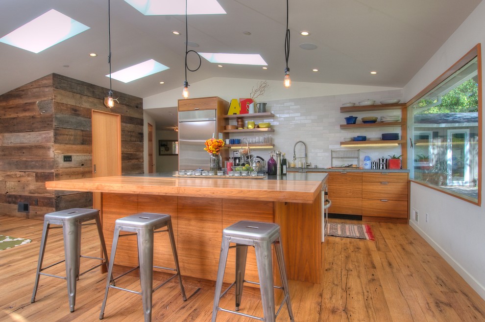 This is an example of a midcentury galley kitchen in San Francisco with flat-panel cabinets, medium wood cabinets, wood benchtops, white splashback, subway tile splashback and stainless steel appliances.