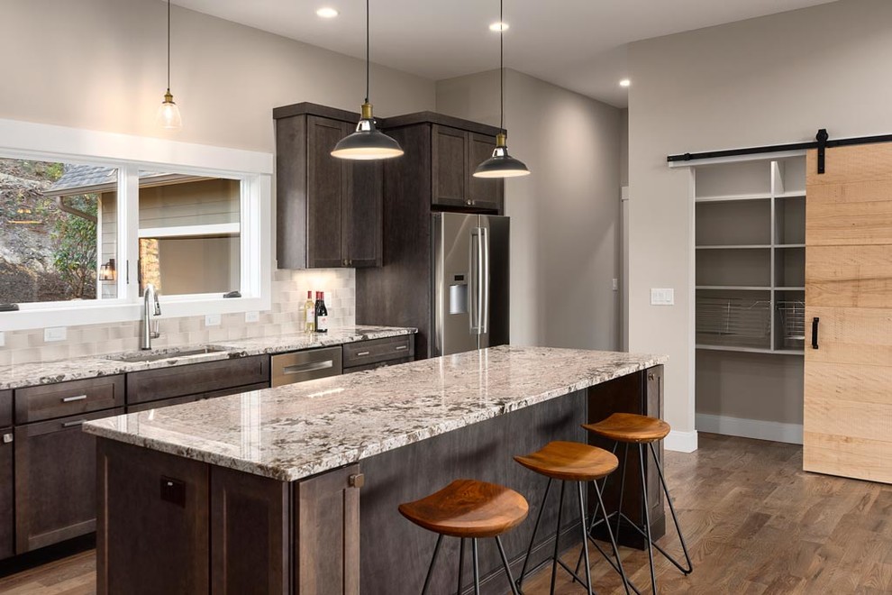 Mid-sized mountain style l-shaped light wood floor eat-in kitchen photo with an undermount sink, recessed-panel cabinets, dark wood cabinets, granite countertops, gray backsplash, ceramic backsplash, stainless steel appliances and an island