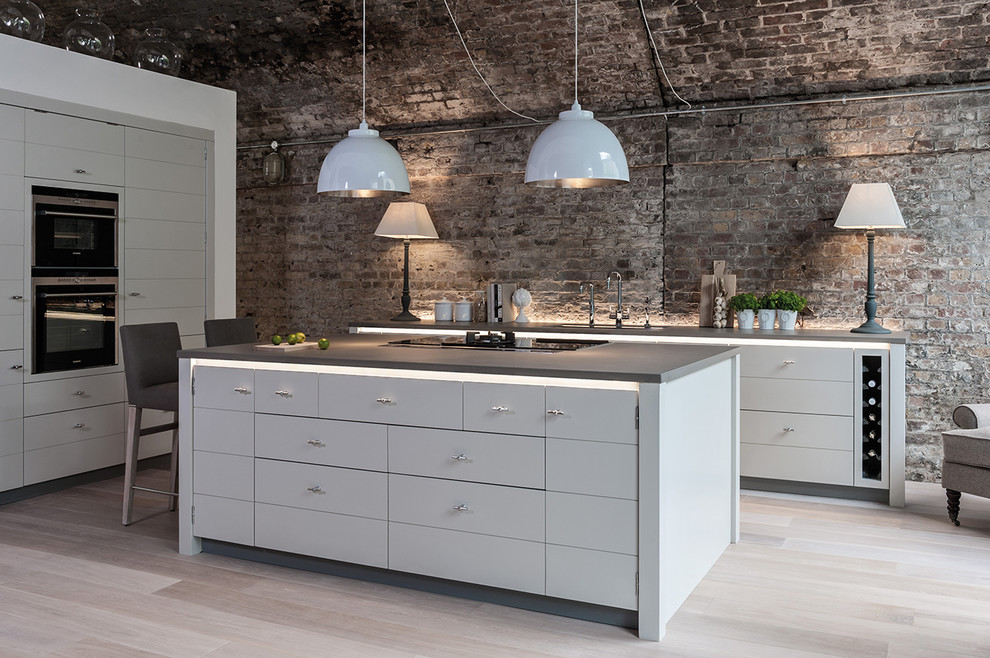 Large industrial l-shaped open plan kitchen in Nantes with an undermount sink, flat-panel cabinets, grey cabinets, brown splashback, brick splashback, black appliances, light hardwood floors, with island and beige floor.