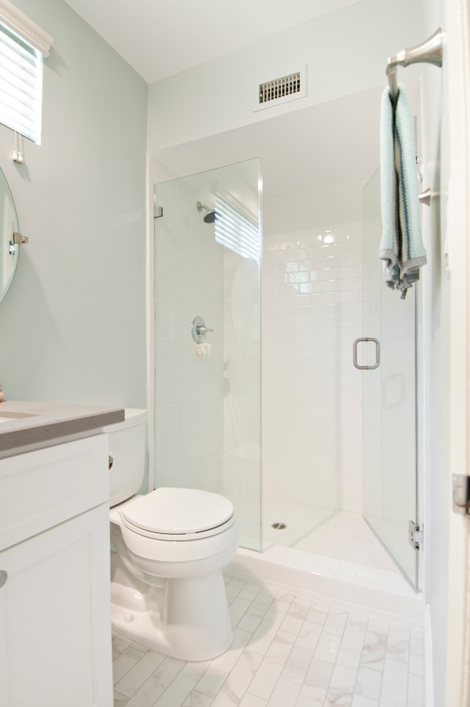 This is an example of a mid-sized transitional master bathroom in Los Angeles with shaker cabinets, white cabinets, an alcove shower, a two-piece toilet, white tile, ceramic tile, blue walls, marble floors, an undermount sink, quartzite benchtops, white floor, a hinged shower door and grey benchtops.