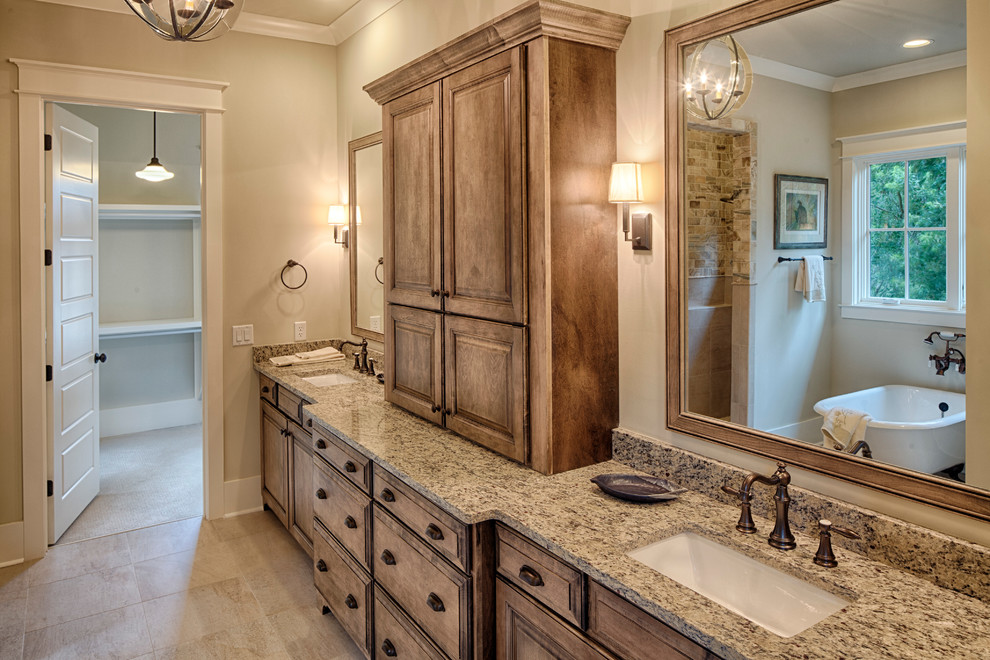 This is an example of a large traditional master bathroom in Charleston with an undermount sink, beaded inset cabinets, medium wood cabinets, granite benchtops, a claw-foot tub, an alcove shower, a one-piece toilet, beige tile, subway tile, beige walls and slate floors.