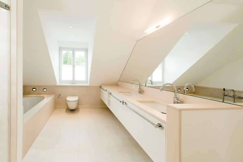 Badezimmer mit Badewanne in Nische, Wandtoilette, beigen Fliesen, weißer Wandfarbe, flächenbündigen Schrankfronten, Steinfliesen, Kalkstein und Trogwaschbecken in Dusseldorf