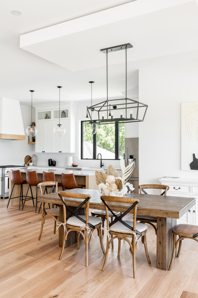 This is an example of an expansive country kitchen/dining combo in Vancouver with white walls, light hardwood floors, a hanging fireplace, a metal fireplace surround and beige floor.