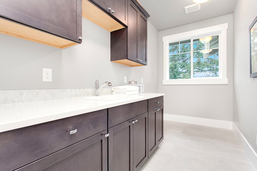 This is an example of a large transitional single-wall dedicated laundry room in Seattle with an utility sink, flat-panel cabinets, dark wood cabinets, quartz benchtops, grey walls and a side-by-side washer and dryer.