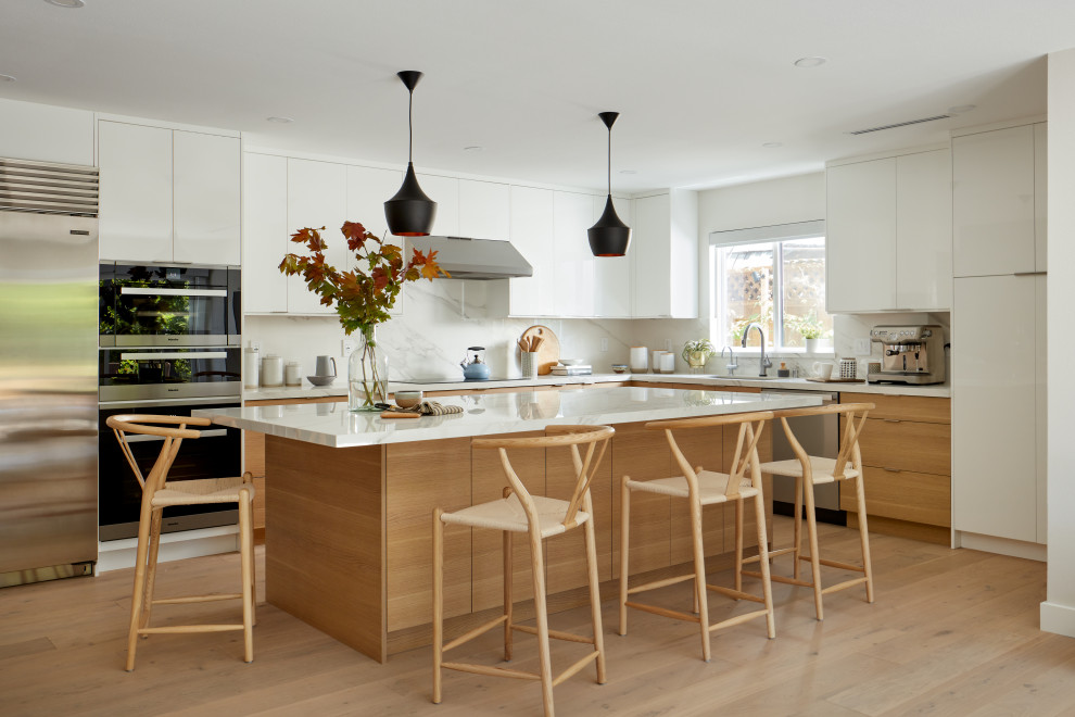 This is an example of a large midcentury l-shaped eat-in kitchen in San Francisco with an undermount sink, flat-panel cabinets, brown cabinets, quartz benchtops, white splashback, porcelain splashback, stainless steel appliances, light hardwood floors, with island and white benchtop.