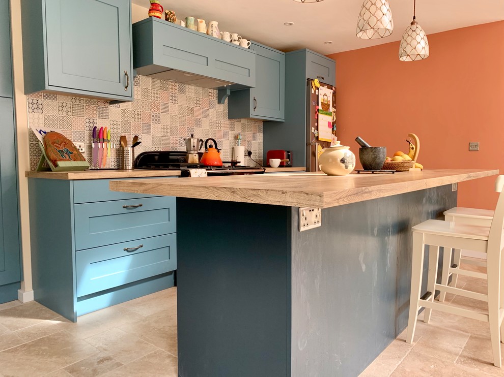 Inspiration for a mid-sized eclectic l-shaped eat-in kitchen in Buckinghamshire with shaker cabinets, blue cabinets, laminate benchtops, multi-coloured splashback, ceramic splashback, travertine floors and with island.