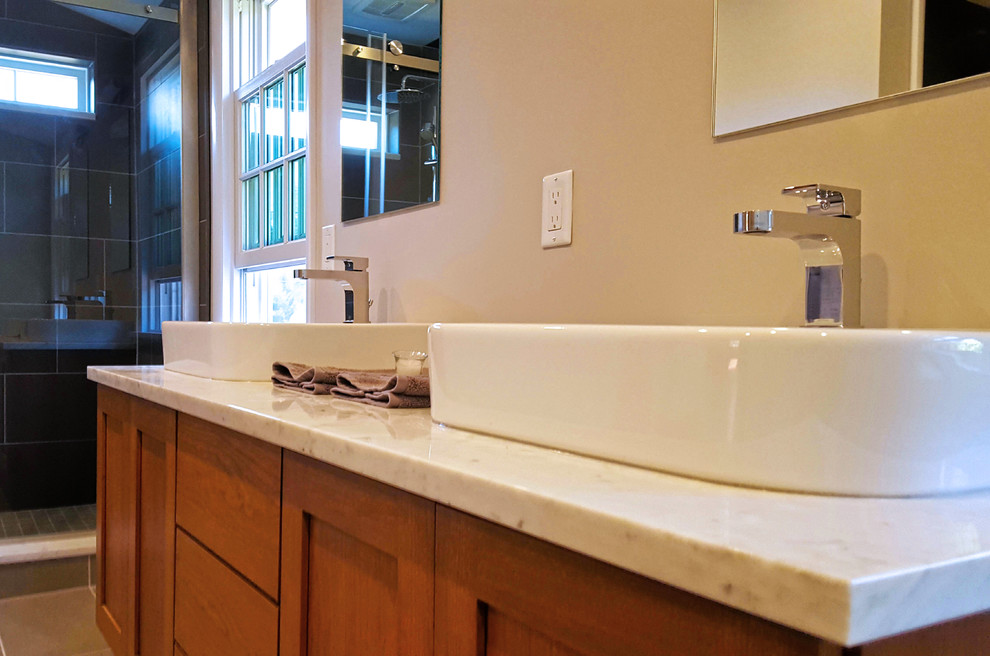 Inspiration for a mid-sized transitional master porcelain tile and brown floor alcove shower remodel with shaker cabinets, medium tone wood cabinets, a vessel sink, beige walls, a hinged shower door and white countertops