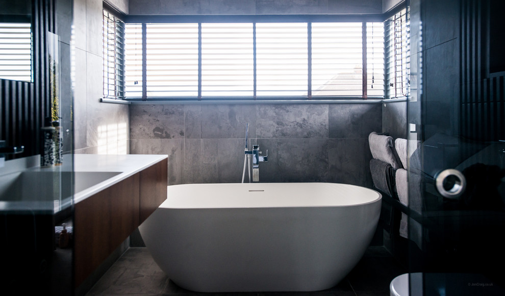 Inspiration for a small contemporary master bathroom in Other with beaded inset cabinets, dark wood cabinets, a freestanding tub, a wall-mount toilet, gray tile, ceramic tile, grey walls, ceramic floors, an integrated sink and engineered quartz benchtops.