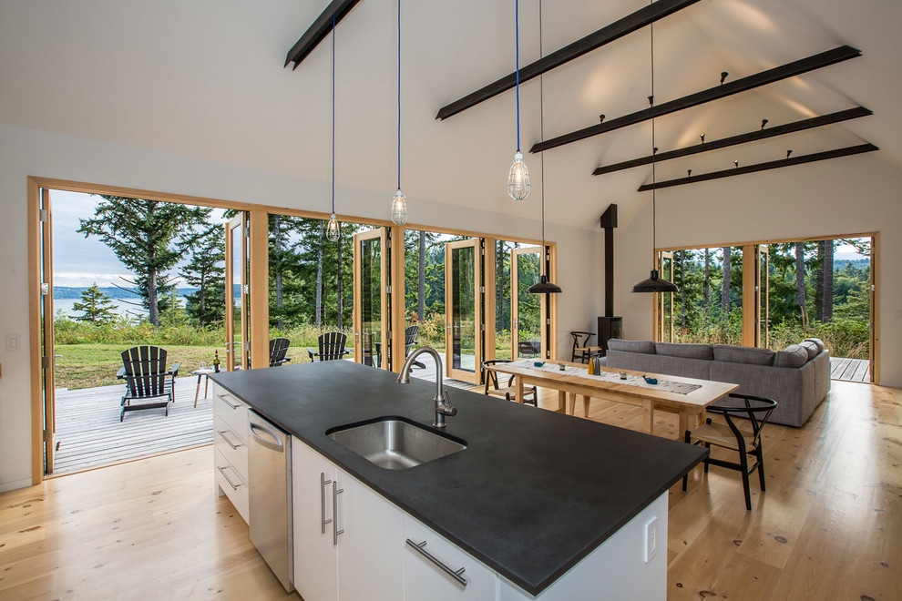 This is an example of a country open plan kitchen in Seattle with an undermount sink, flat-panel cabinets, white cabinets, solid surface benchtops, stainless steel appliances, light hardwood floors and with island.