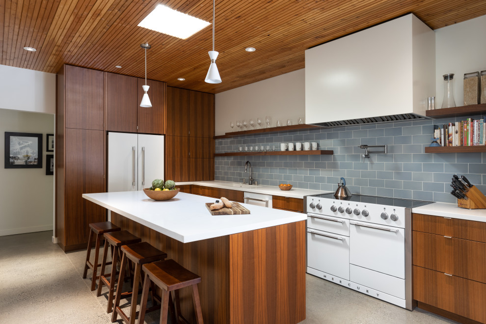 Inspiration for a contemporary galley concrete floor, gray floor and exposed beam eat-in kitchen remodel in San Francisco with medium tone wood cabinets, solid surface countertops, ceramic backsplash, white countertops, flat-panel cabinets, blue backsplash, white appliances and an island