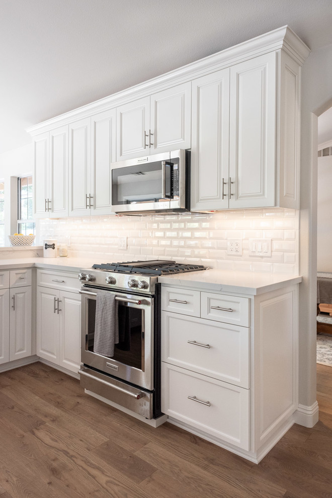 This is an example of a mid-sized country u-shaped eat-in kitchen in San Luis Obispo with a drop-in sink, raised-panel cabinets, white cabinets, quartz benchtops, white splashback, subway tile splashback, stainless steel appliances, laminate floors, a peninsula, brown floor and yellow benchtop.