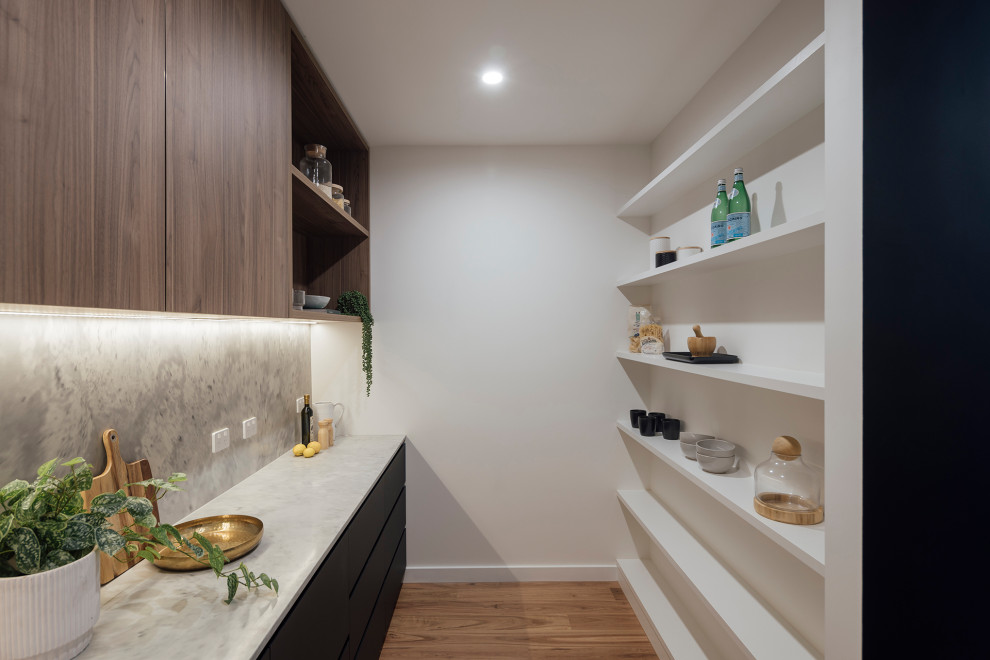 Design ideas for a mid-sized contemporary galley kitchen pantry in Melbourne with solid surface benchtops, black appliances, medium hardwood floors and with island.