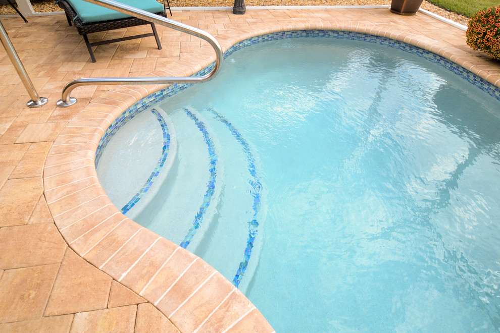 Inspiration for a backyard custom-shaped pool in Miami with concrete pavers.