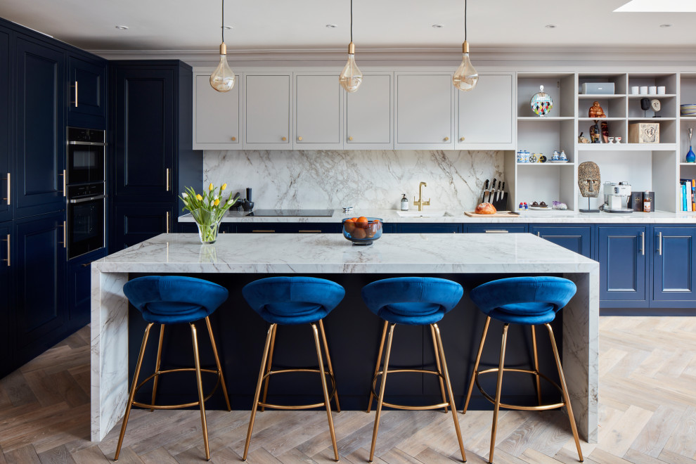 Design ideas for a large transitional l-shaped kitchen in London with blue cabinets, marble benchtops, white splashback, marble splashback, panelled appliances, light hardwood floors, with island, white benchtop, an undermount sink, recessed-panel cabinets and beige floor.