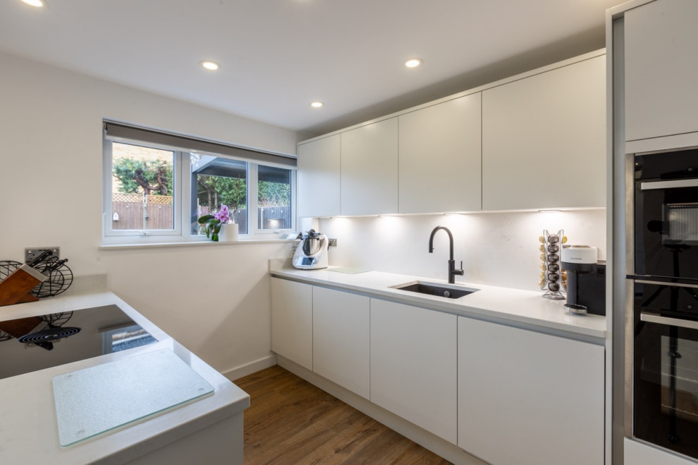 This is an example of a small contemporary galley open plan kitchen in Sussex with flat-panel cabinets, white cabinets, quartz worktops, white splashback, engineered quartz splashback, a breakfast bar and white worktops.
