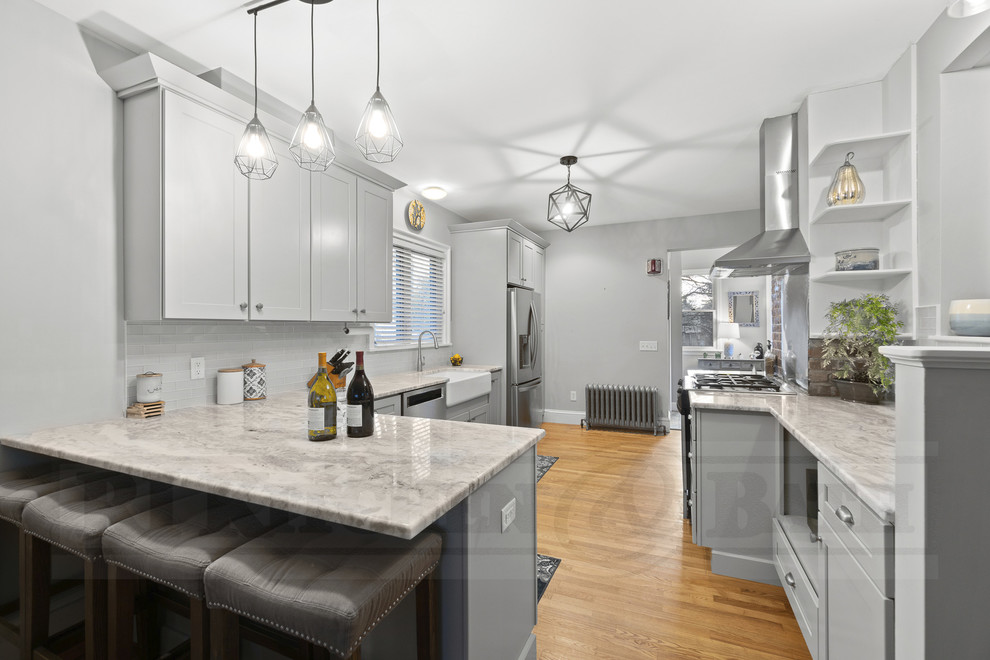 Eat-in kitchen - transitional medium tone wood floor eat-in kitchen idea in Providence with a farmhouse sink, shaker cabinets, gray cabinets, glass tile backsplash and a peninsula